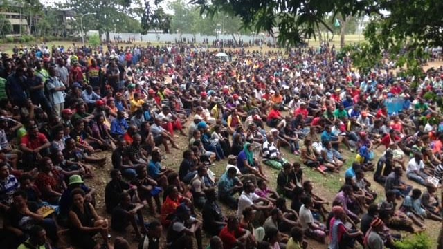 Thousands of University of Papua New Guinea students sit out on the grass.