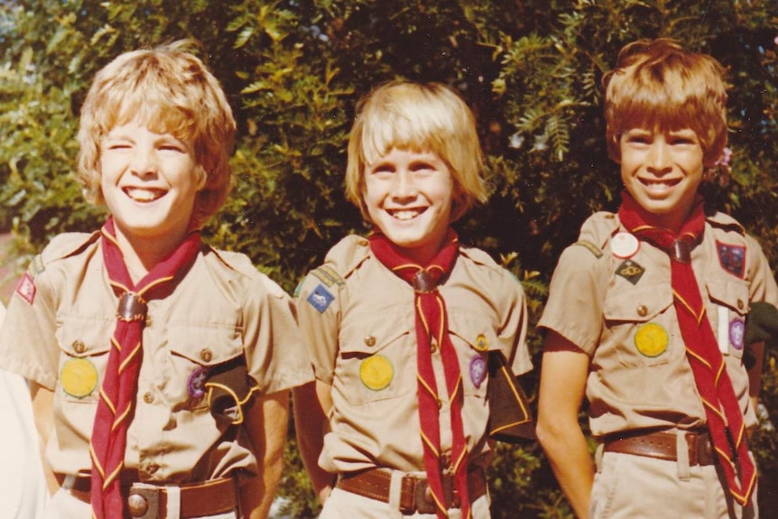 Three boys wearing Cubs and Scouts uniforms grin at the camera in 1977.
