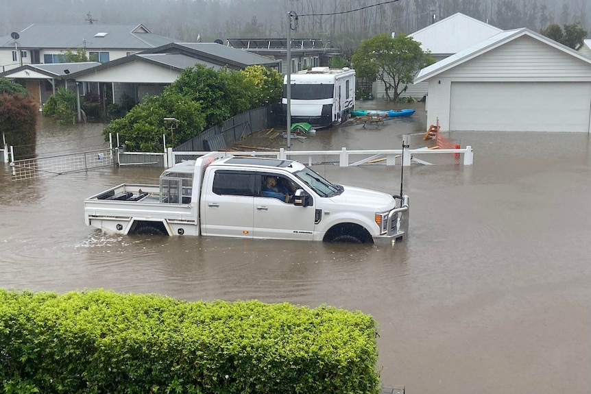 A ute submerged almost to the top of its wheel-wells on a flooded residential street.