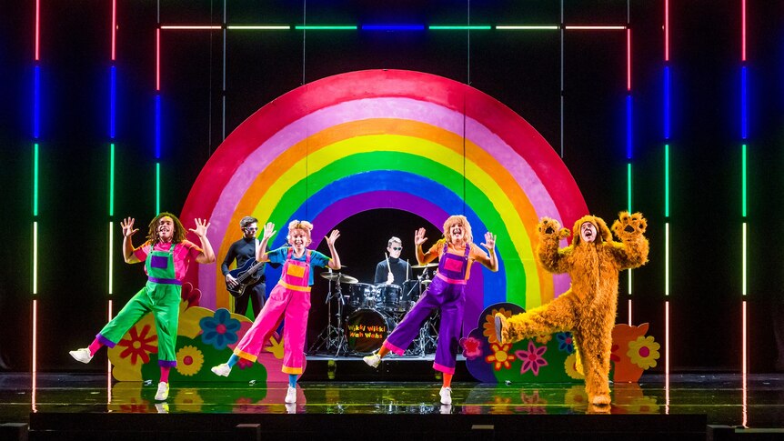 Four costumed children's entertainers on a stage with a rainbow and colourful lights decorating the stage