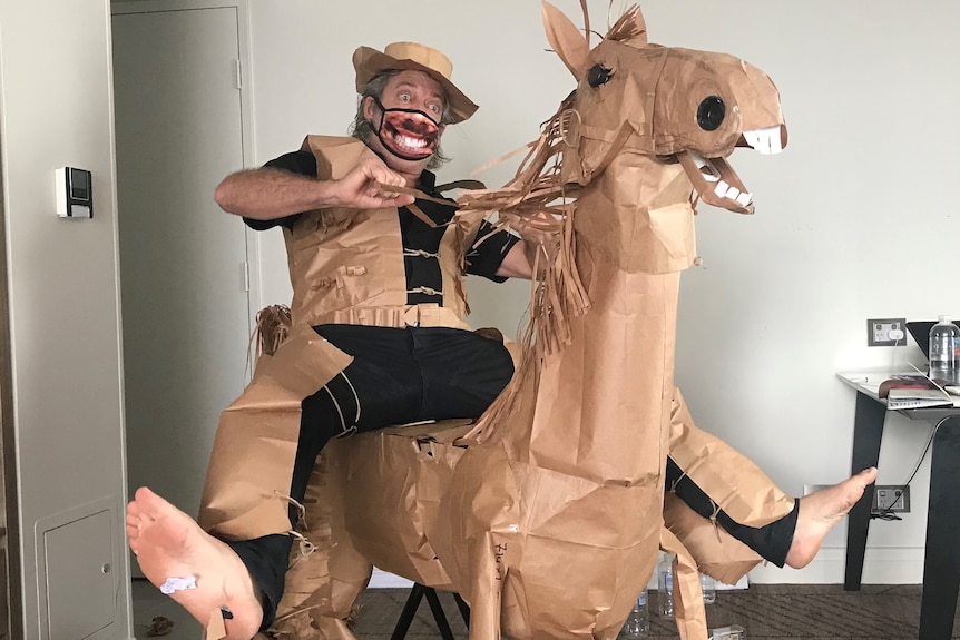 A man in a paper cowboy costume rides a horse constructed from various materials.
