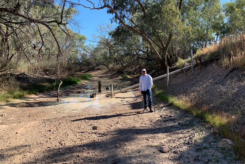 A man stands in a dry river bed with just a puddle of water behind him.