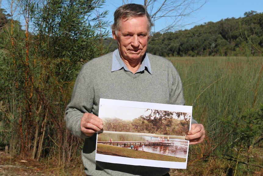 David Hunt standing in front of the dried lake holding a historical photo when the lake was full.