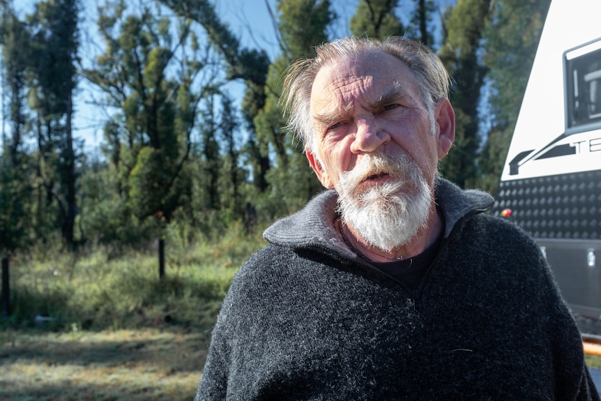 A man with a grey beard outside a caravan