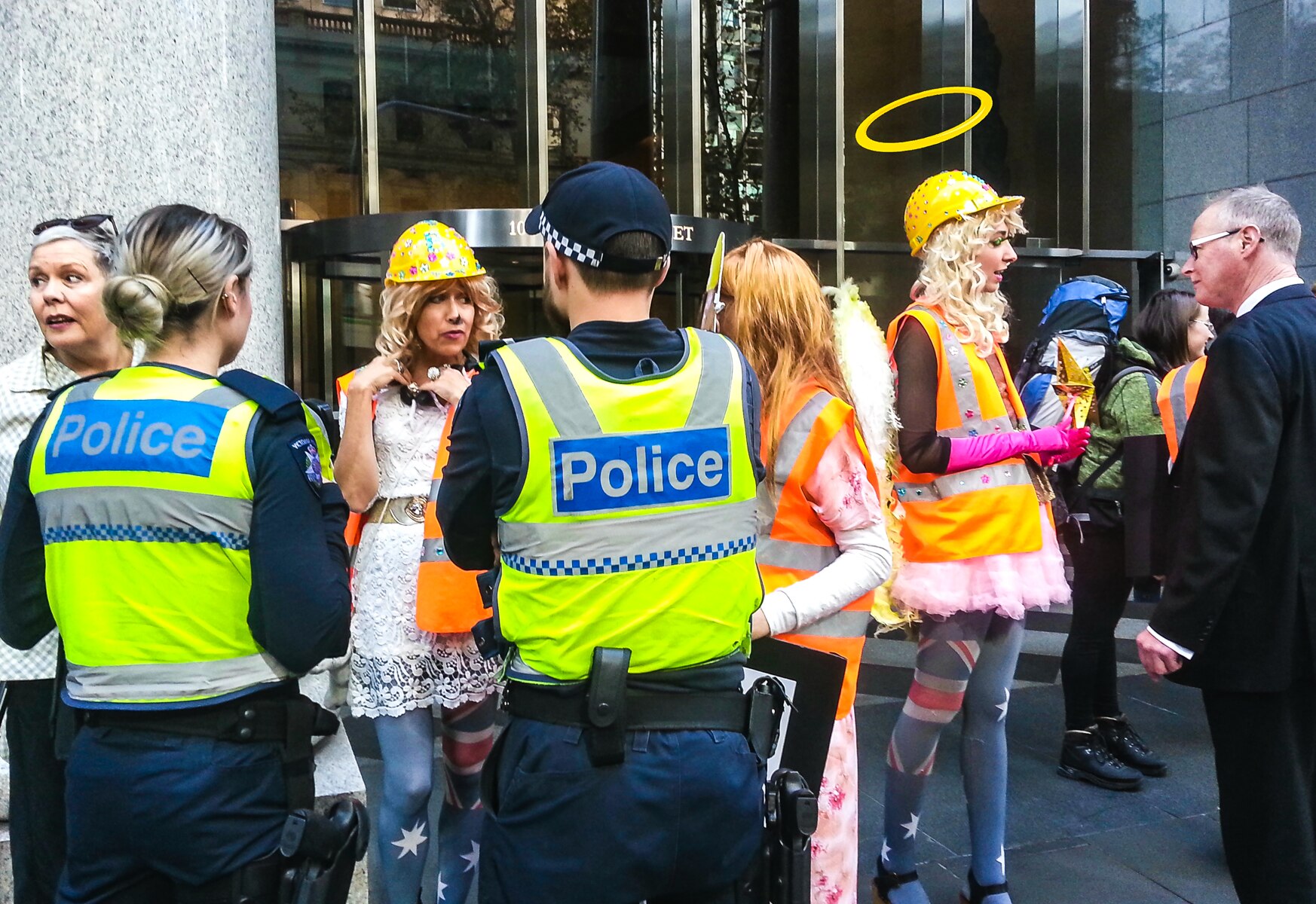 A group of protestors in high vis clothing speaking to police outside an office building