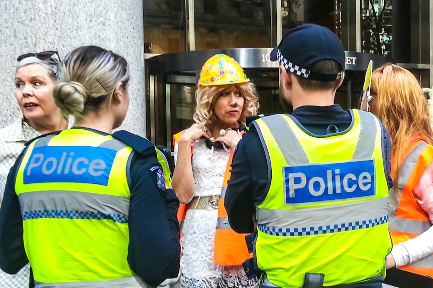 A group of protestors in high vis clothing speaking to police outside an office building