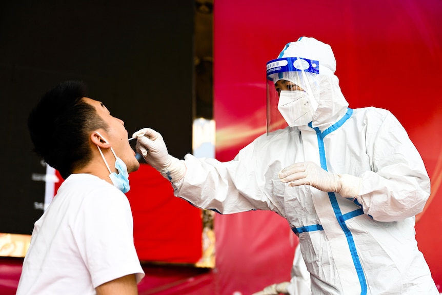 A woman in full PPE sticks a swab down a man's throat 