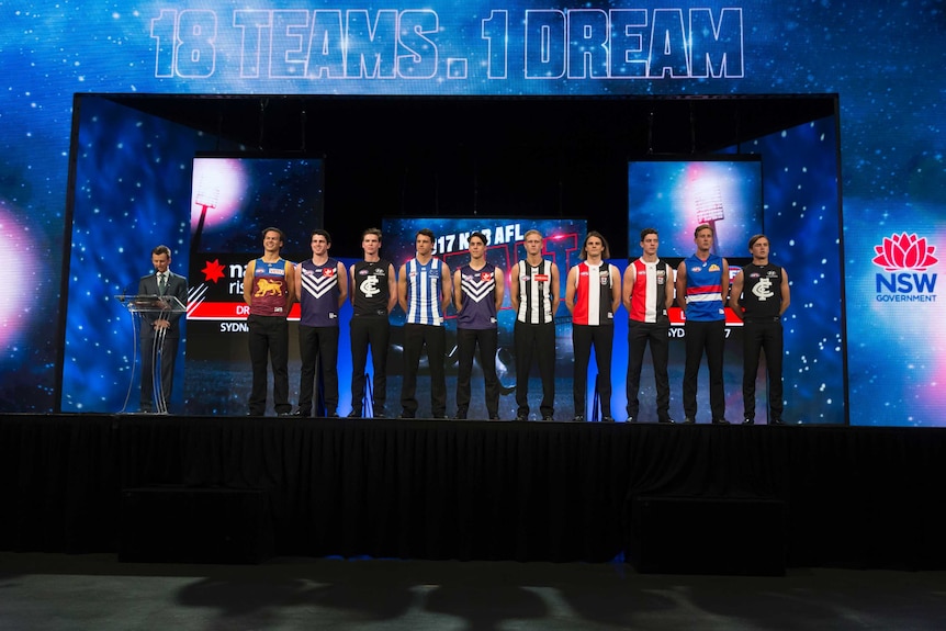 A row of players stand on a stage next to a man at a podium.
