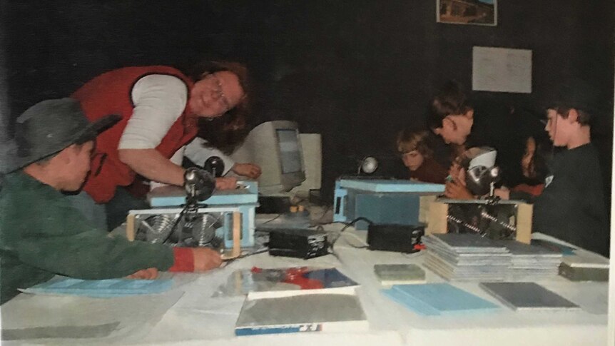 A woman and several children gather around a desk examining broadcast technology.