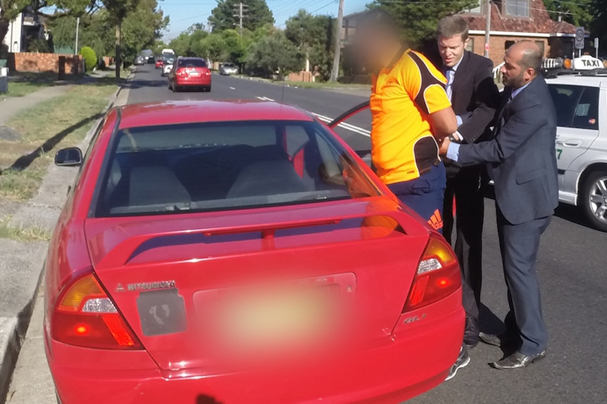 Two detectives in suits handcuff a man in an orange shirt on a suburban street