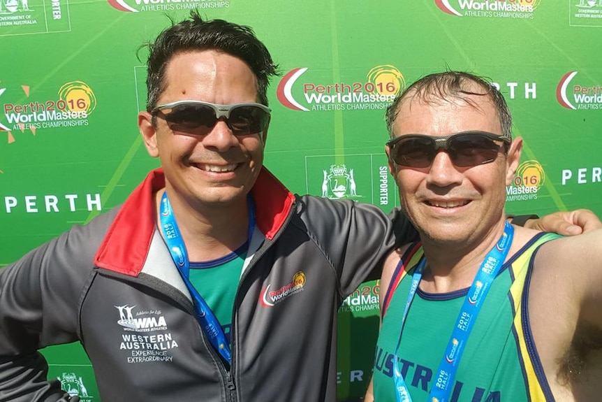 Two men arm in arm in athletic gear after a run, with medals around their necks. 