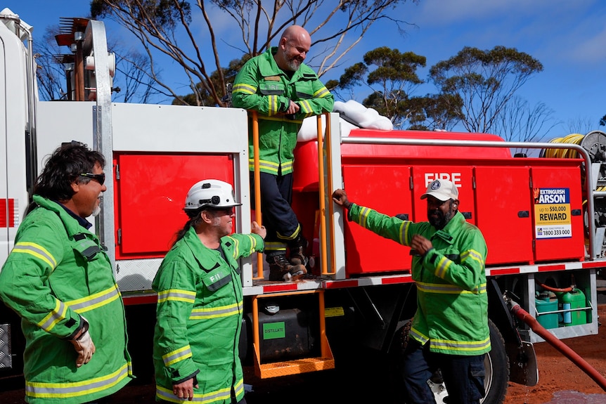 A group of smiling firefighters standing around a truck in the desert.