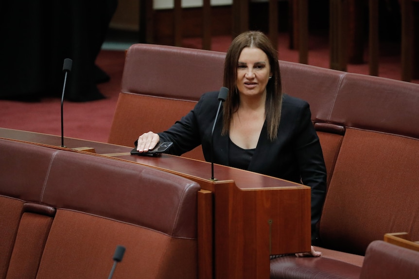 Jacqui Lambie, wearing a black blazer, sits in the senate with her hand on the table infront of her