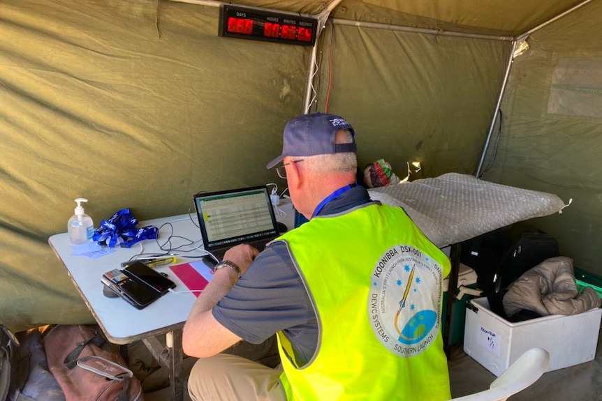 A man looks at a laptop computer in a tent