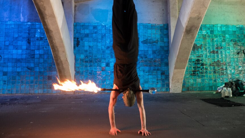 Brett Schmerl does a handstand balancing his fire wand.