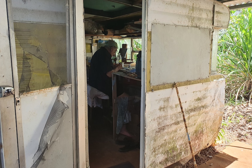 A view from outside looking into a caravan where a man sits at a table painting.