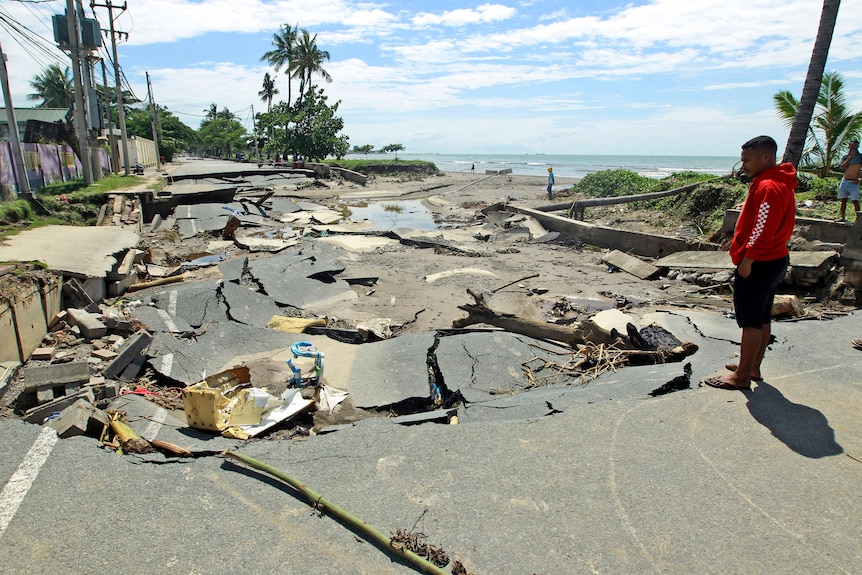 A man ispects a seaside road that has collapsed and been broken apart by heavy rain and floodwaters.