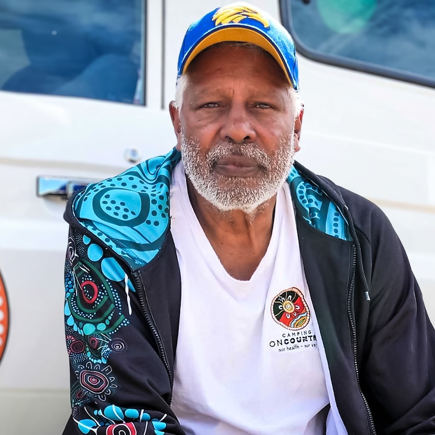 A man leans against a truck with an Inidgenous design and wears a West Coast Eagles cap.