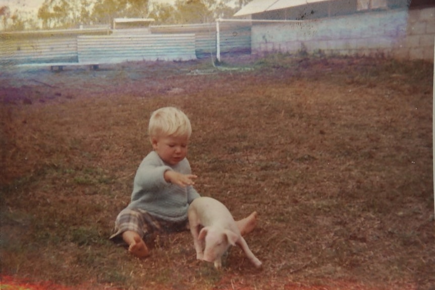 A young boy pictured with a cute piglet in front of the piggery his father built