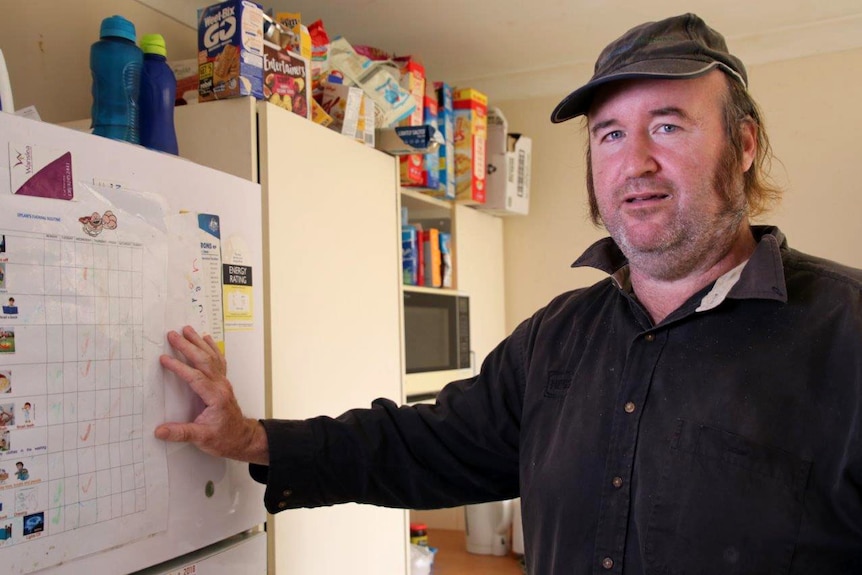 Damian John wearing a cap in front of a planning chart stuck to his fridge.