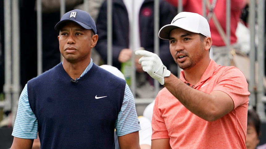 Jason Day points while standing next to Tiger Woods on a golf course.