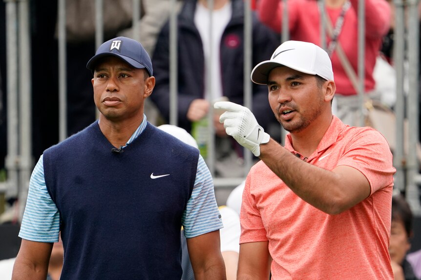 Jason Day points while standing next to Tiger Woods on a golf course.