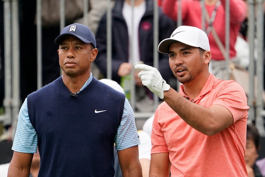 Jason Day points while standing next to Tiger Woods on a golf course.