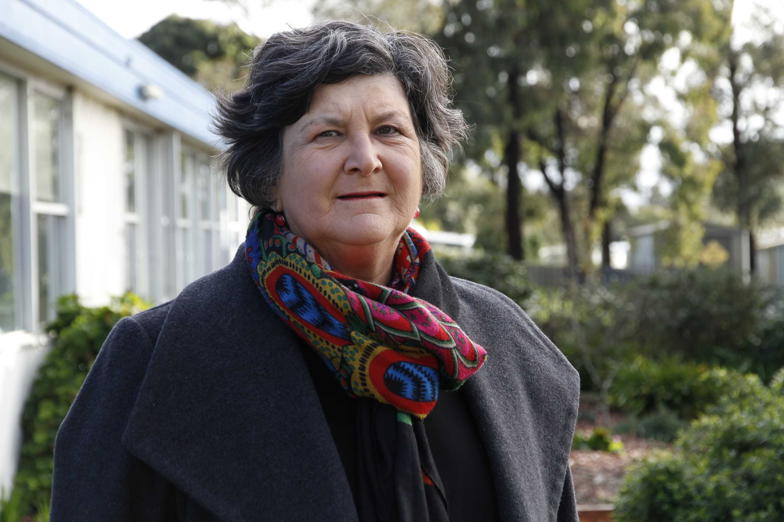 Michelle Wilson stands in front of trees and a building, looking at the camera.