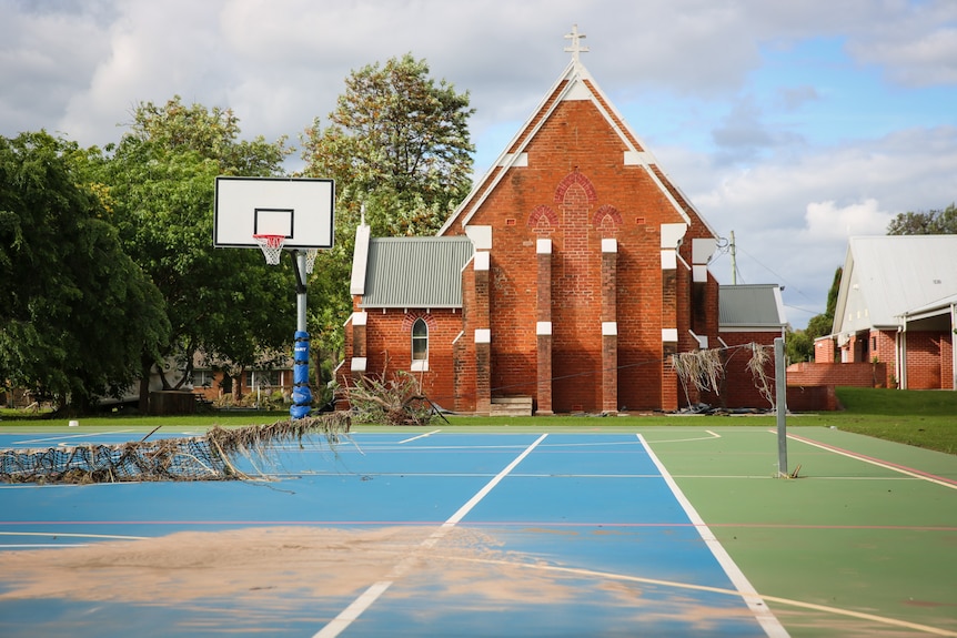 Green and blue outdoor basketball court, a red brick church featuring a water mark in the background
