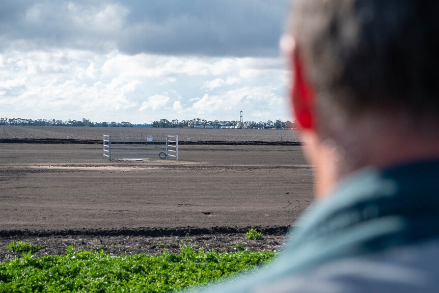 A photo over a man's shoulder of a csg drill rig operating in the distance.