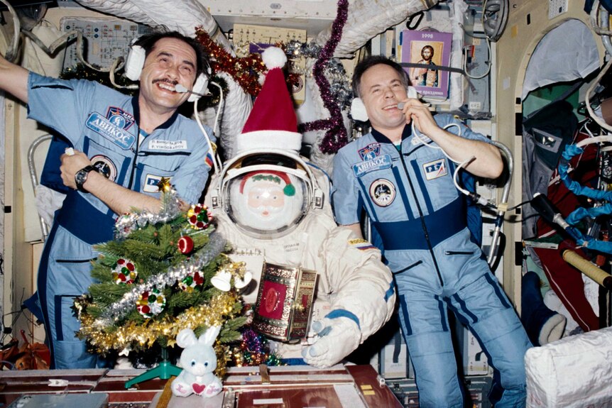 Two men smiling in blue space suits on a space station