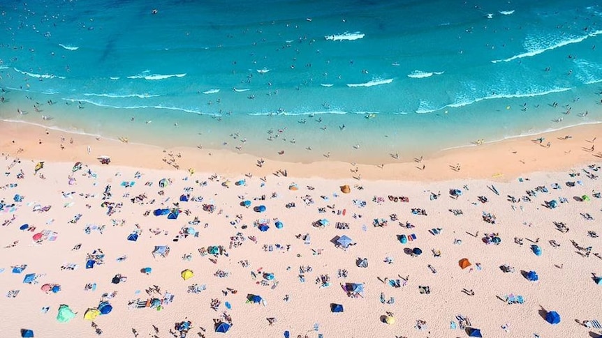 An aerial view of a crowded beach with clear, aqua water.