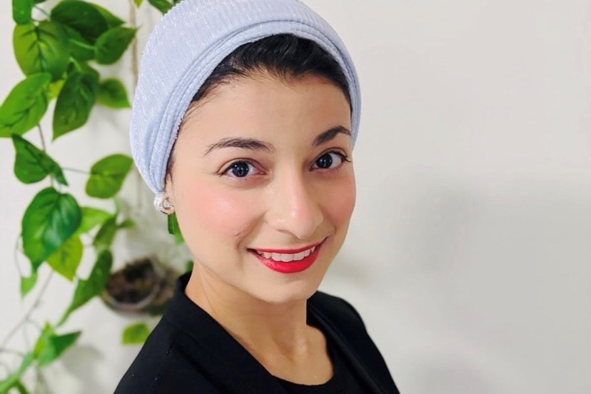 a woman with a blue headscarf and bright pink lipstick smiles directly at the camera
