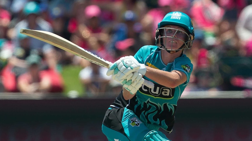 Beth Mooney in Brisbane Heat colours — a bright teal cricket uniform with helmet and pads — swings her bat and looks to the sky.