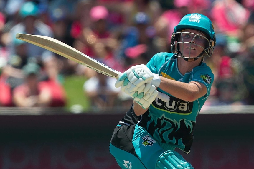 Beth Mooney in Brisbane Heat colours — a bright teal cricket uniform with helmet and pads — swings her bat and looks to the sky.