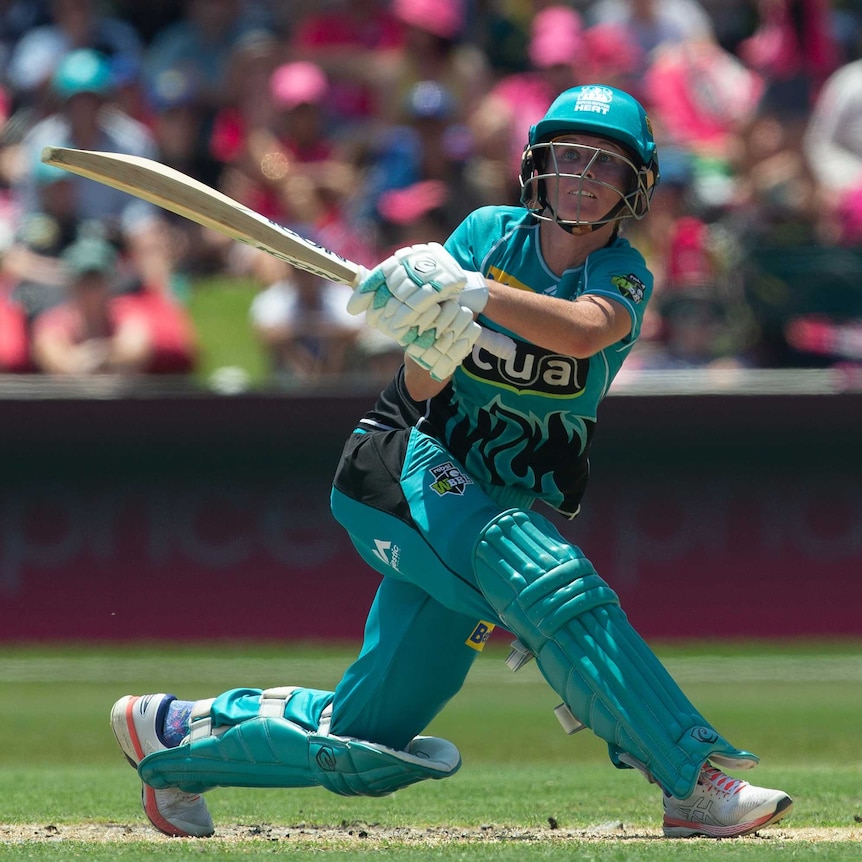 Beth Mooney in Brisbane Heat colours — a bright teal cricket uniform with helmet and pads — swings her bat and looks to the sky.