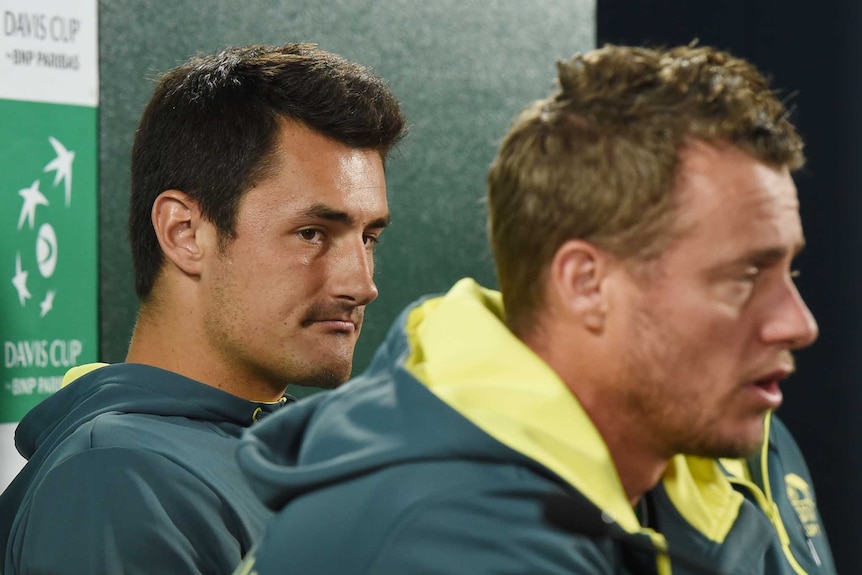 Bernard Tomic looks at Lleyton Hewitt as he speaks during a Davis Cup press conference. Nick Kyrgios is sitting nearby.