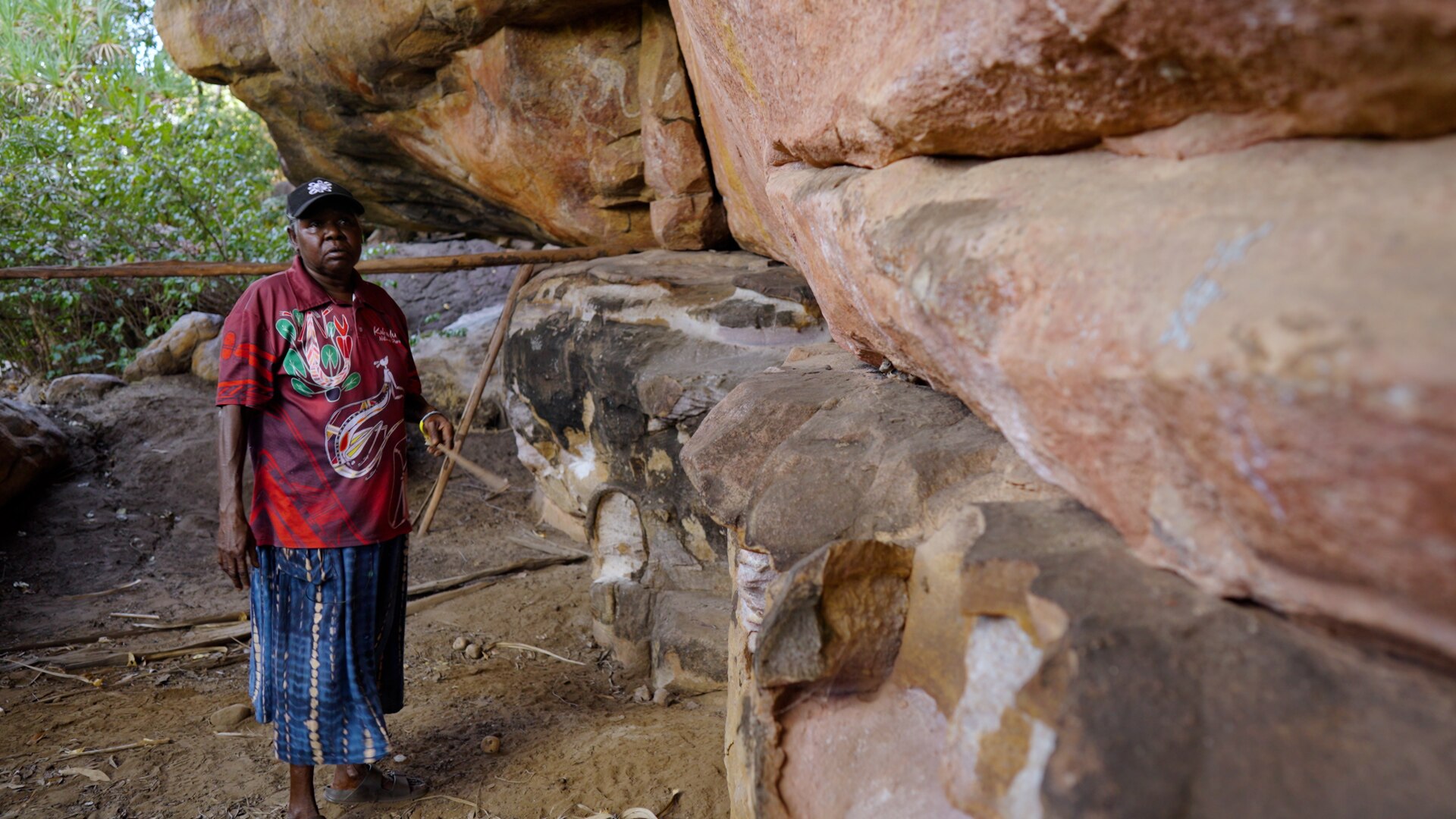 Indigenous woman Merrill Girrabul stands next to rock art