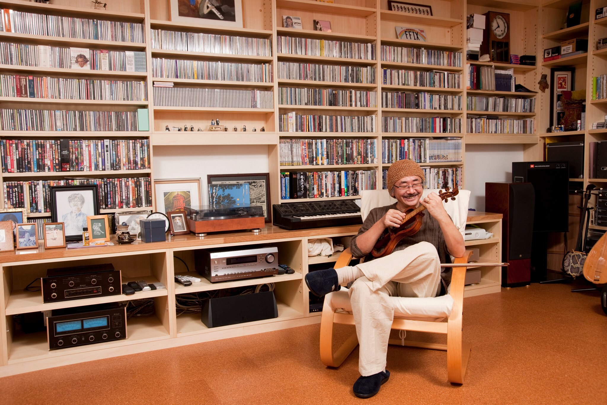 Japanese composer Nobuo Umeatsu sits playing viola in a lounge surrounded by cds and musical equipment