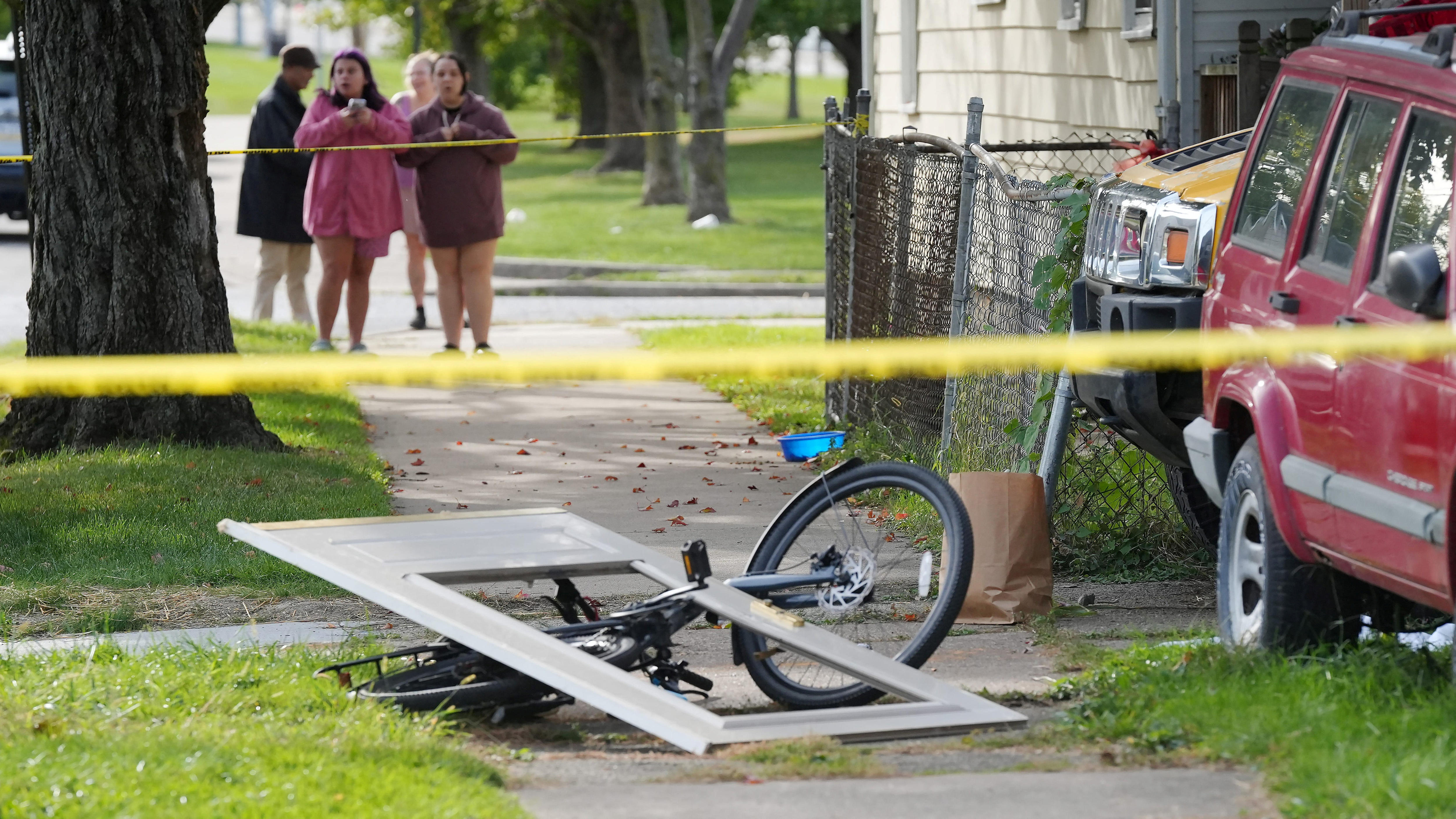 Four people stand behind yellow police tape.