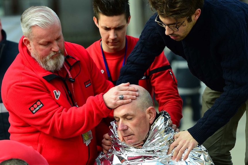 A man wrapped in a silver blanket is being attended to by medics.