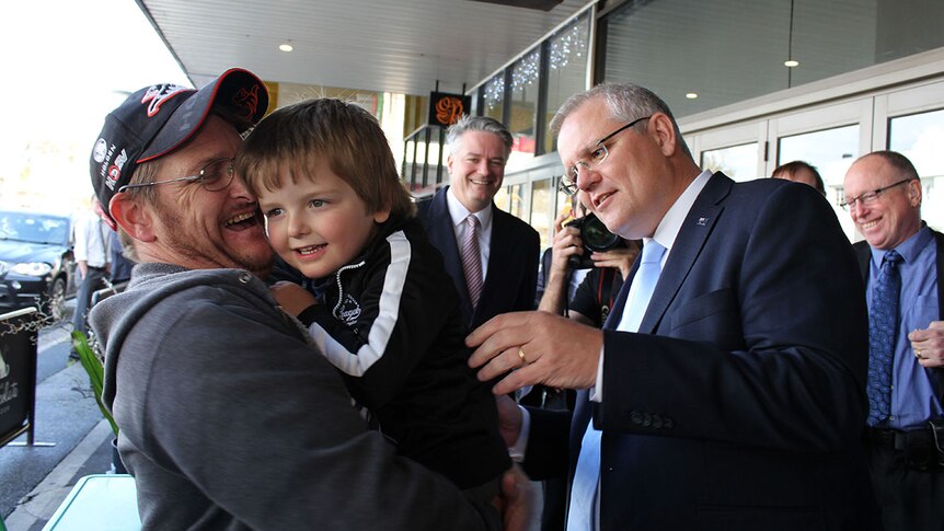 Prime Minister Scott Morrison puts his hand out to a young boy and his dad.