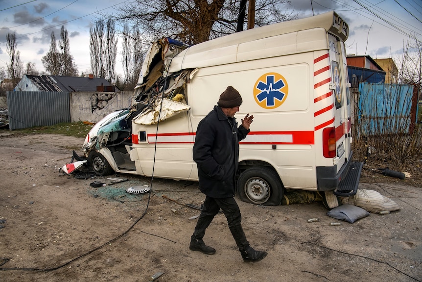 A man walks past a damaged ambulance.