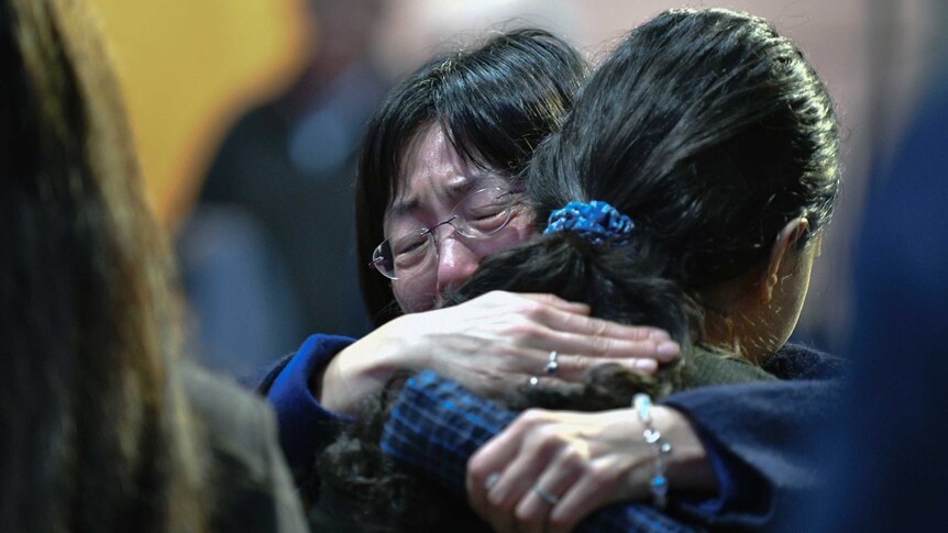 Two women embrace while crying at a memorial.