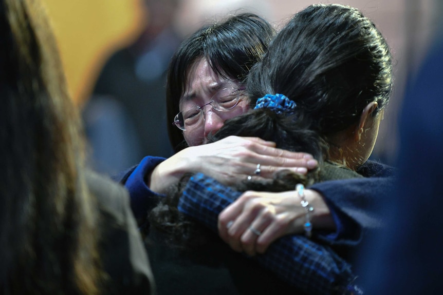 Two women embrace while crying at a memorial.