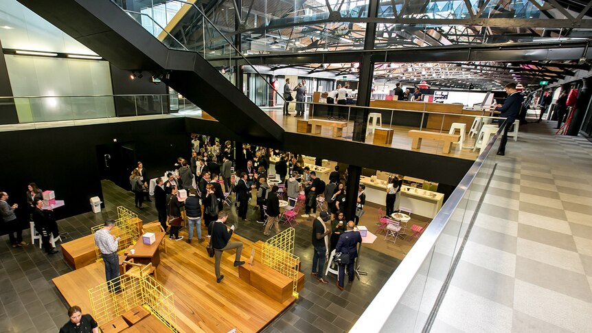 Inside a vast, two-storey converted warehouse with business people milling around tables and chairs.
