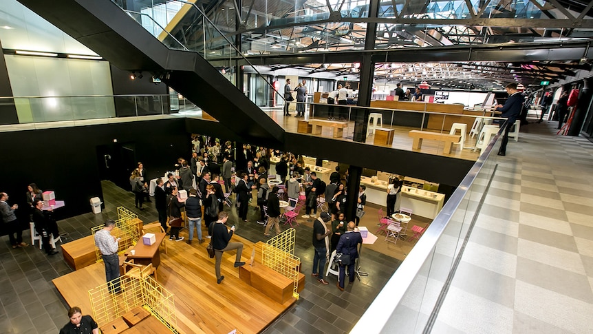 Inside a vast, two-storey converted warehouse with business people milling around tables and chairs.