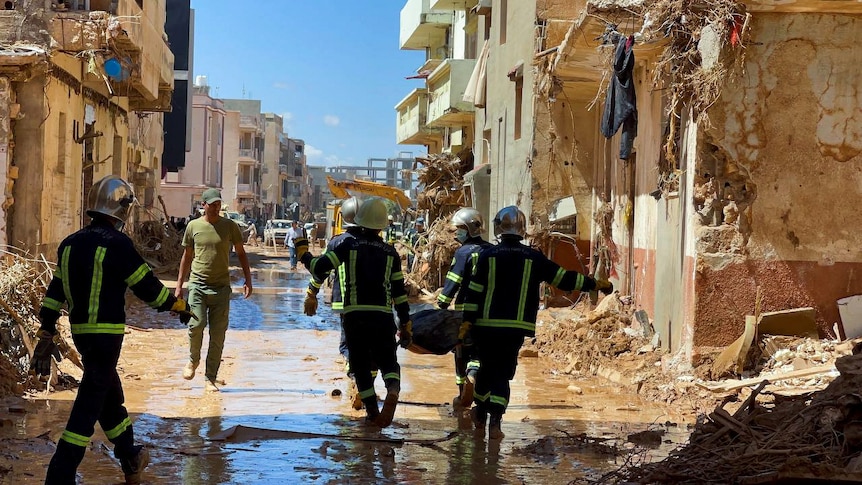 Rescuers carry a dead body down a street with destroyed buildings on both sides