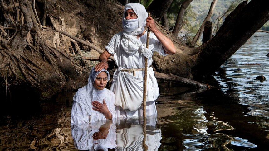 A Mandaean women dressed in traditional clothing  is baptised by a priest in the Nepean river in Penrith.