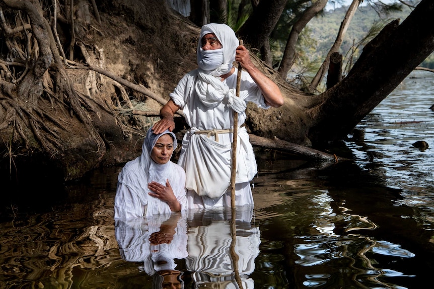 A Mandaean women dressed in traditional clothing  is baptised by a priest in the Nepean river in Penrith.